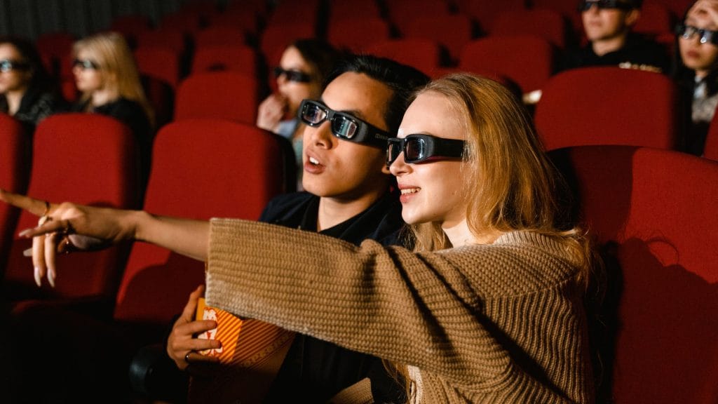 Nieoczywiste filmy na deszczowe dni 8 Młodzi ludzie, chłopak z dziewczyną w sali kinowej z okularami na oczach pełni emocji zachwytu podczas oglądania filmu.